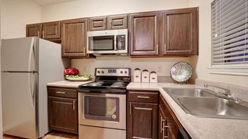 a kitchen with wooden cabinets and stainless steel appliances at Wilson Crossing Apartments in Cedar Hill, Texas